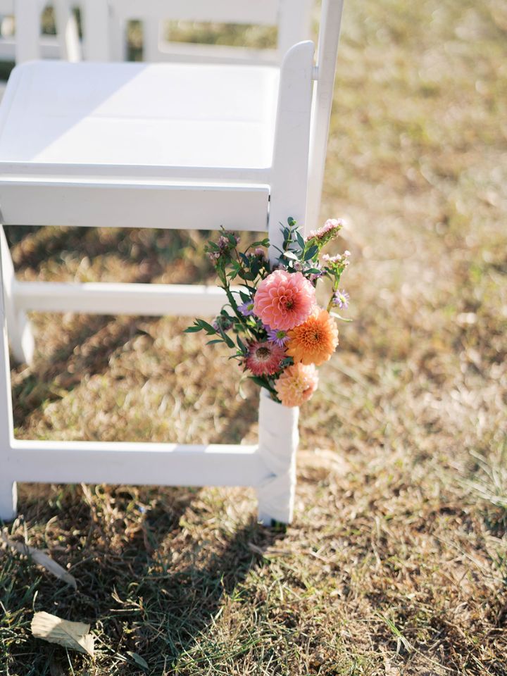 A small flower arrangement on the back of the last chair at a wedding ceremony aisle entrance.