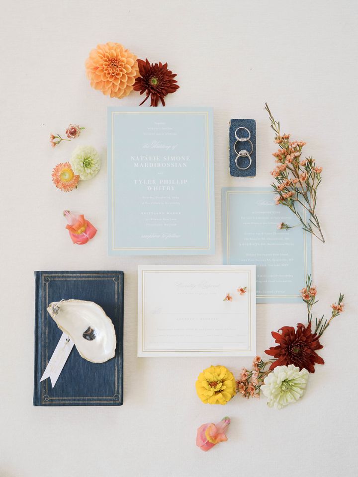 Flatlay style photo of wedding invitation, oyster shell, and flowers.