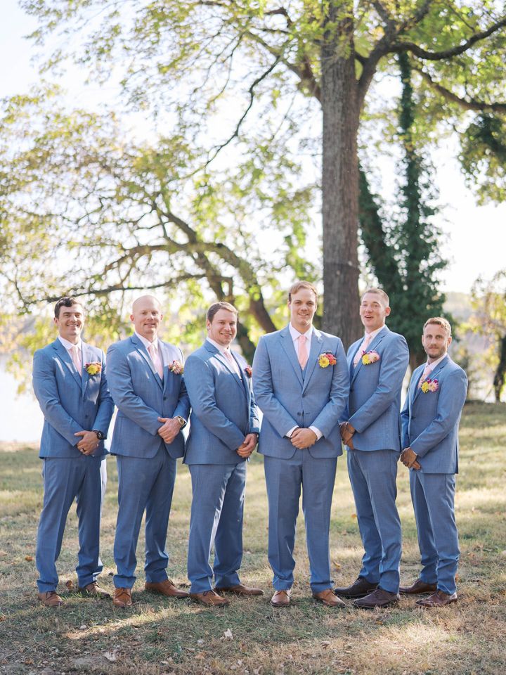 Groom and groomsmen stand in light blue suits with pocket square style fresh flower boutonnieres.