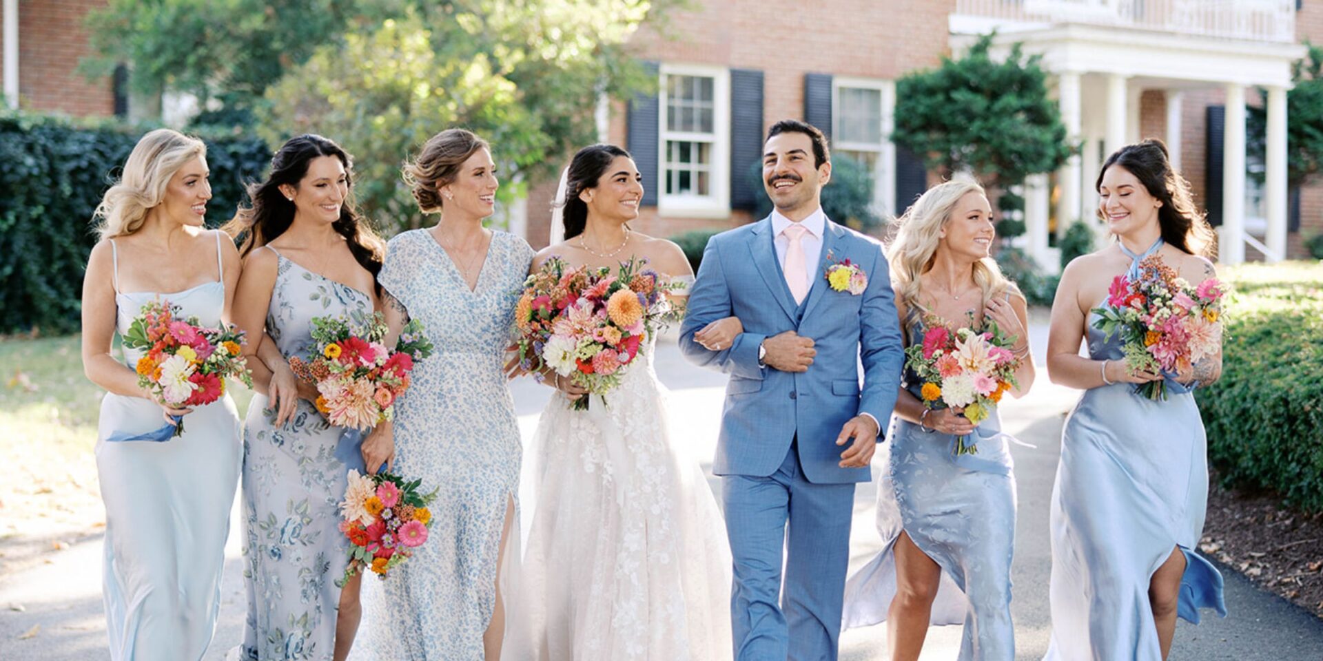 Bride walks with wedding party in front of Brittland Estates manor house.