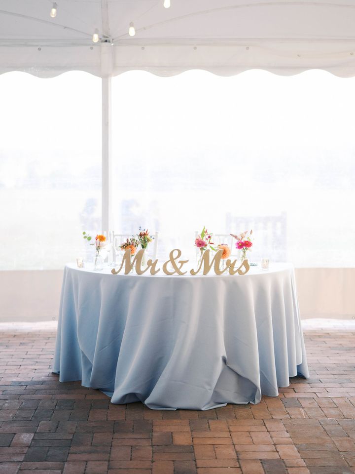 Sweetheart table with a soft blue linen, Mr. & Mrs. sign, and brightly colored flowers in small glass bud vases.