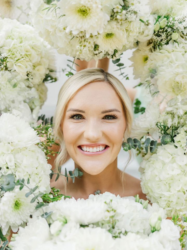 Bride smiles in the center of a "frame" made of white flower bouquets.
