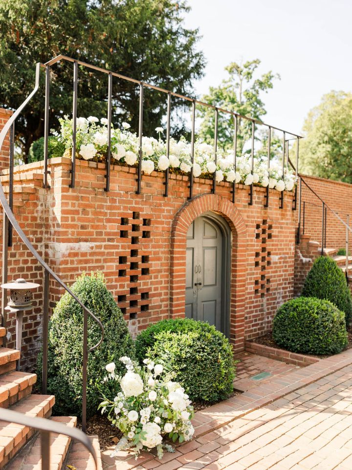 Curved brick staircase at garden entrance with lots of white hydrangea wedding flower arrangements.