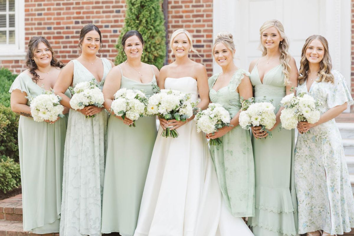 Bridesmaids in seafoam green dresses on either side of bride with white hydrangea wedding bouquets.