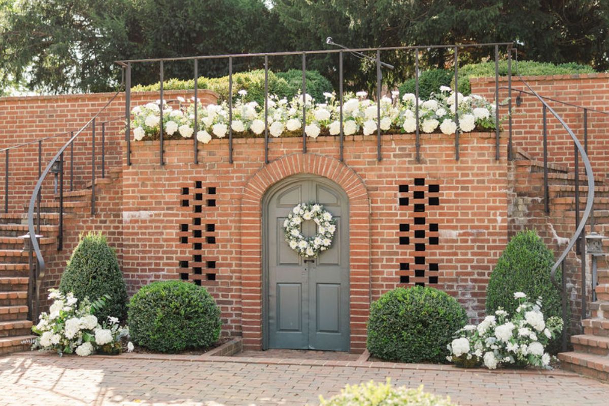Curved brick double staircase leads down to garden, with lots of white hydrangea flower arrangements.