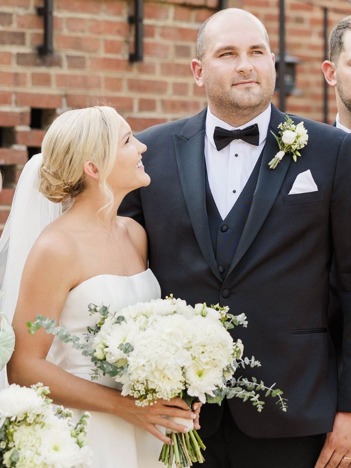Bride smiles up at groom, holding a white bouquet.
