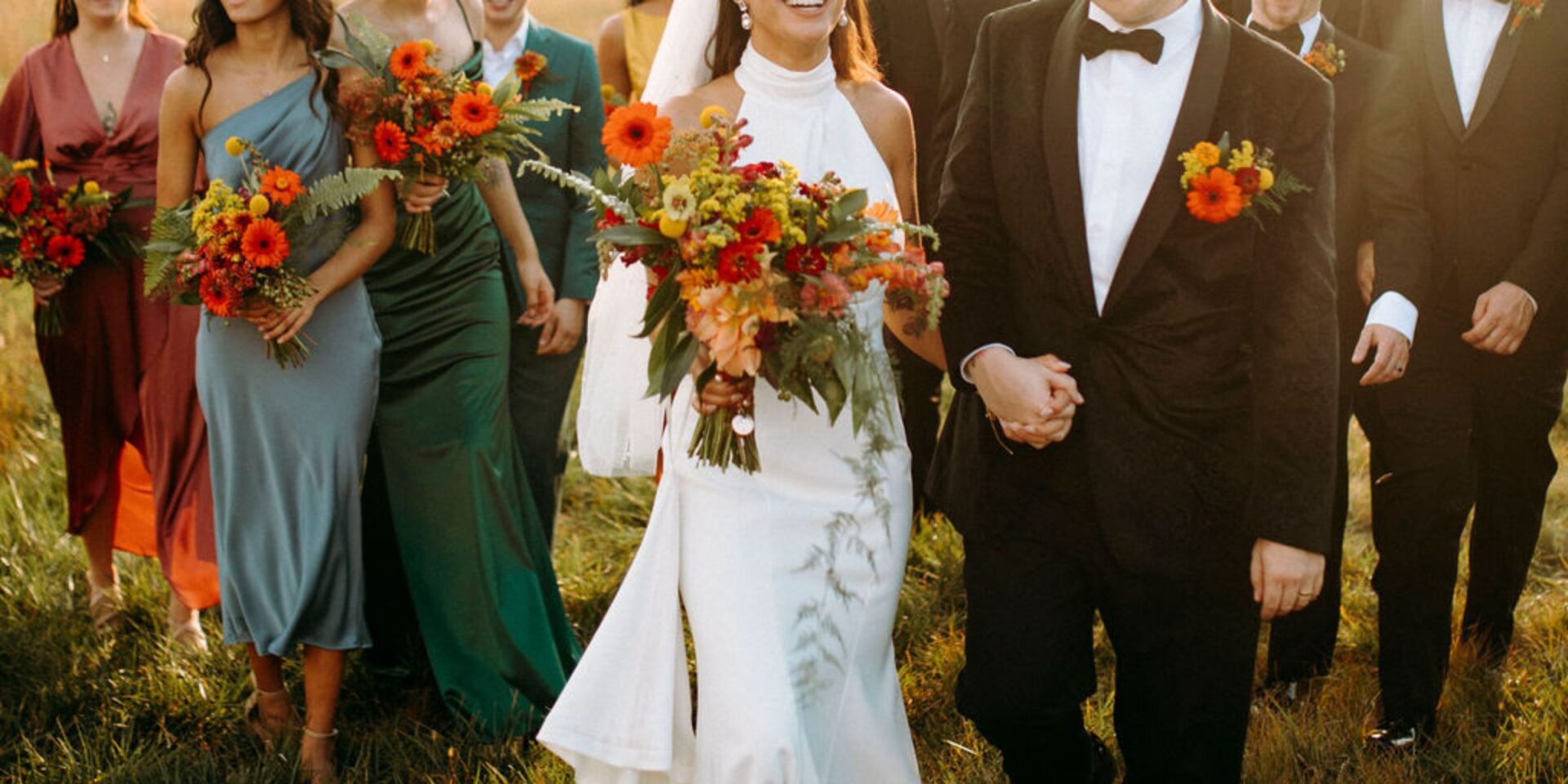 Bride and groom walk in front of wedding party in autumn golden hour sunlight.