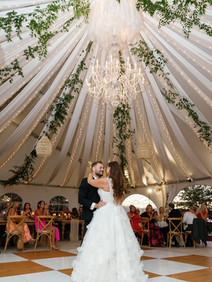 Bride and groom dance under tent ceiling greenery installation.