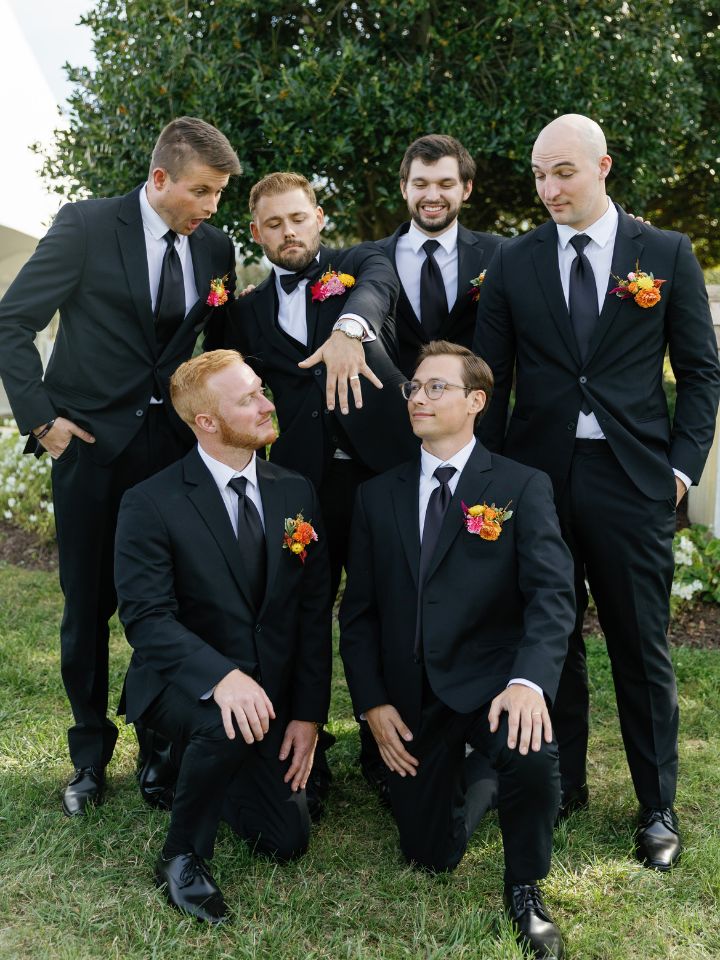 Groom and groomsmen pose in black suits, floral pocket squares.