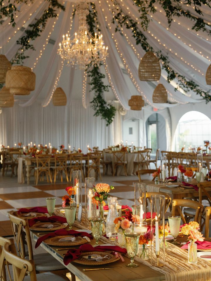 Inside of wedding reception tent with greenery and bud vases.