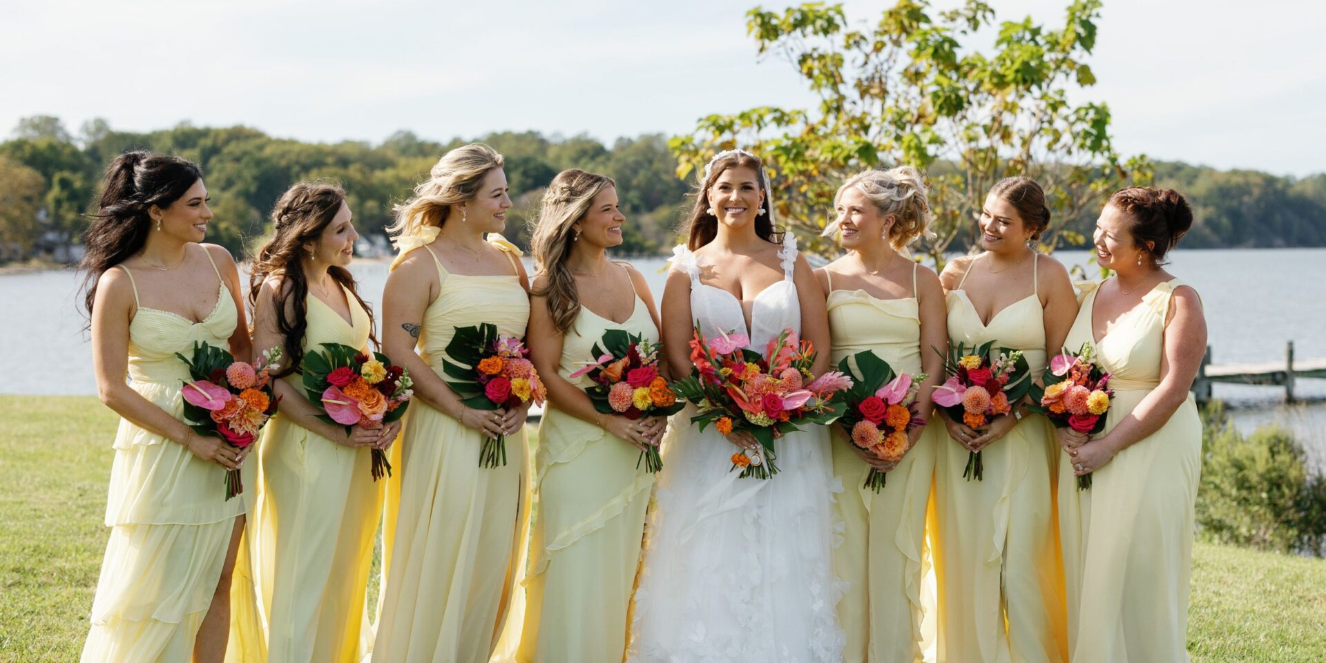 Bride and bridesmaids in butter yellow dresses hold tropical wedding flower bouquets.