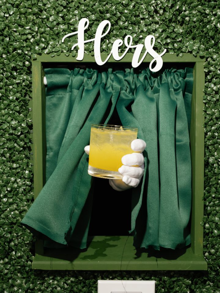 Signature drink wall with white gloved hand serving drinks.