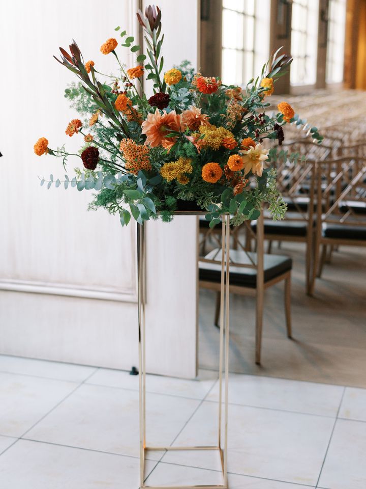 Aisle Pedestal Gold metallic pedestal stand with fall flower arrangement on top.