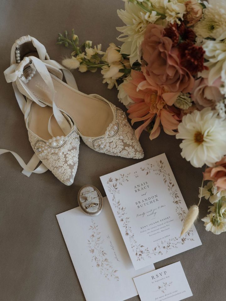 Flatlay photo with wedding invite, shoes, and bouquet in warm fall color wedding palette.