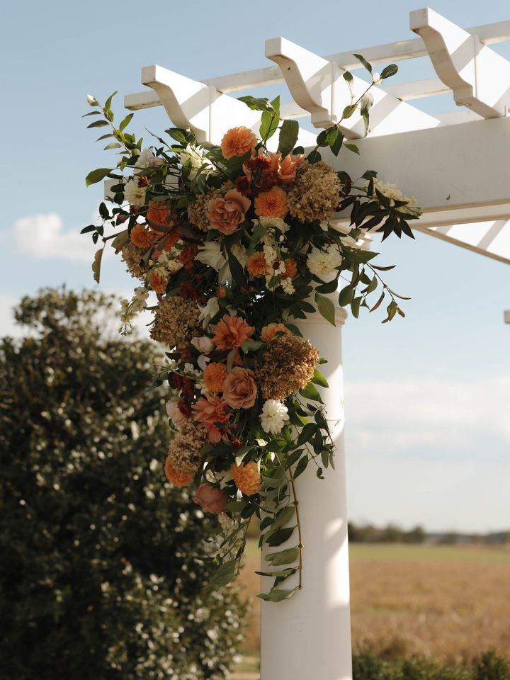Flower arrangement on large white pergola for wedding ceremony.