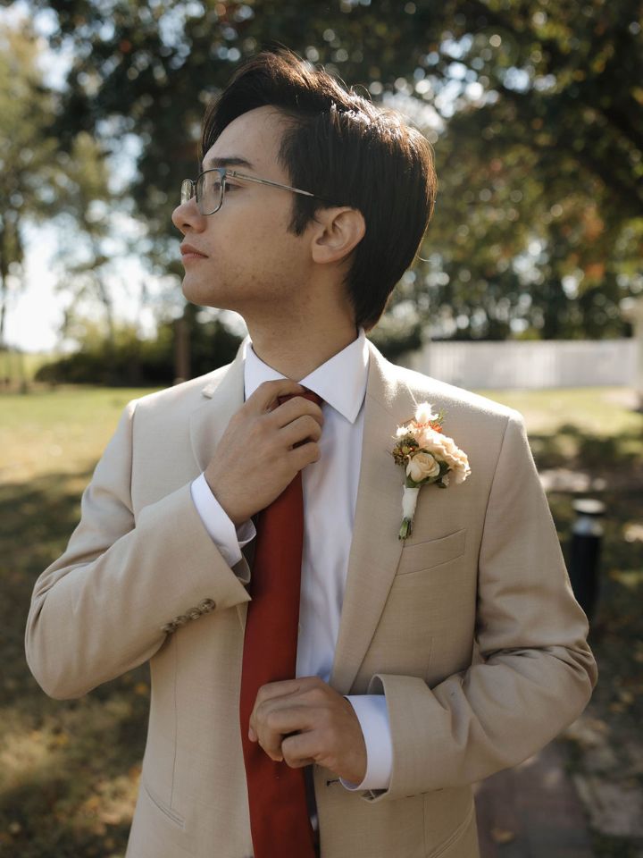 Groom adjusts red tie in tan suit with fall flower boutonniere.