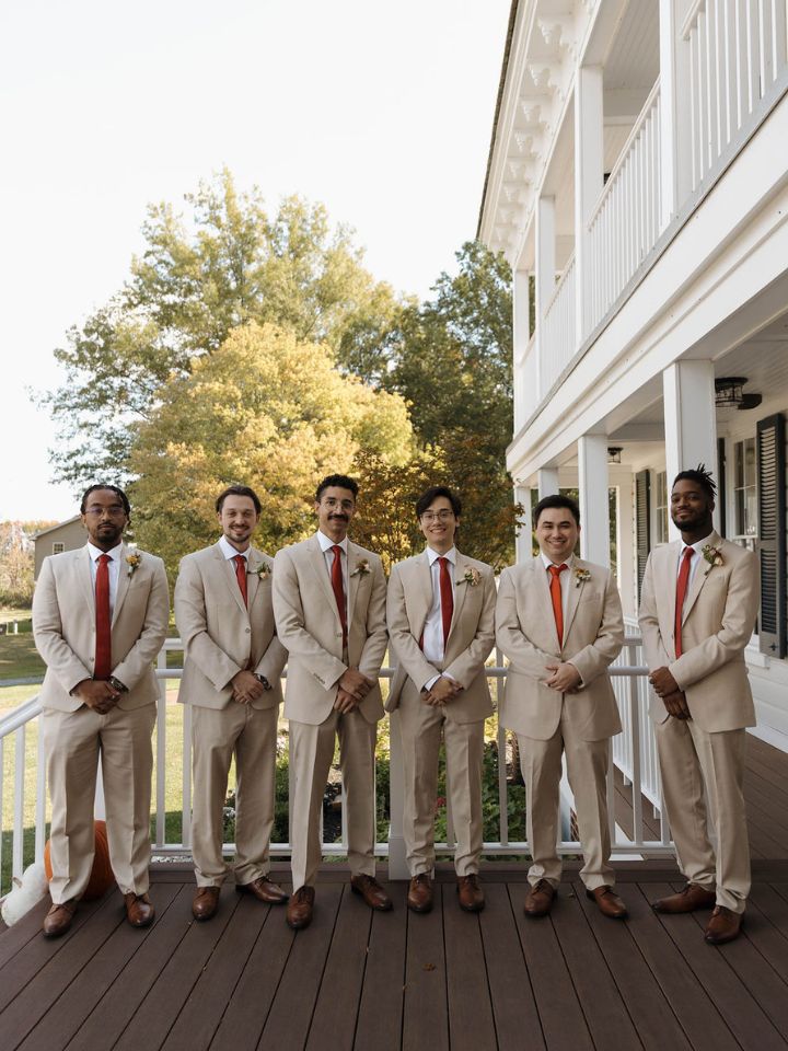 Groom and groomsmen in a line with tan suits and dark red ties.