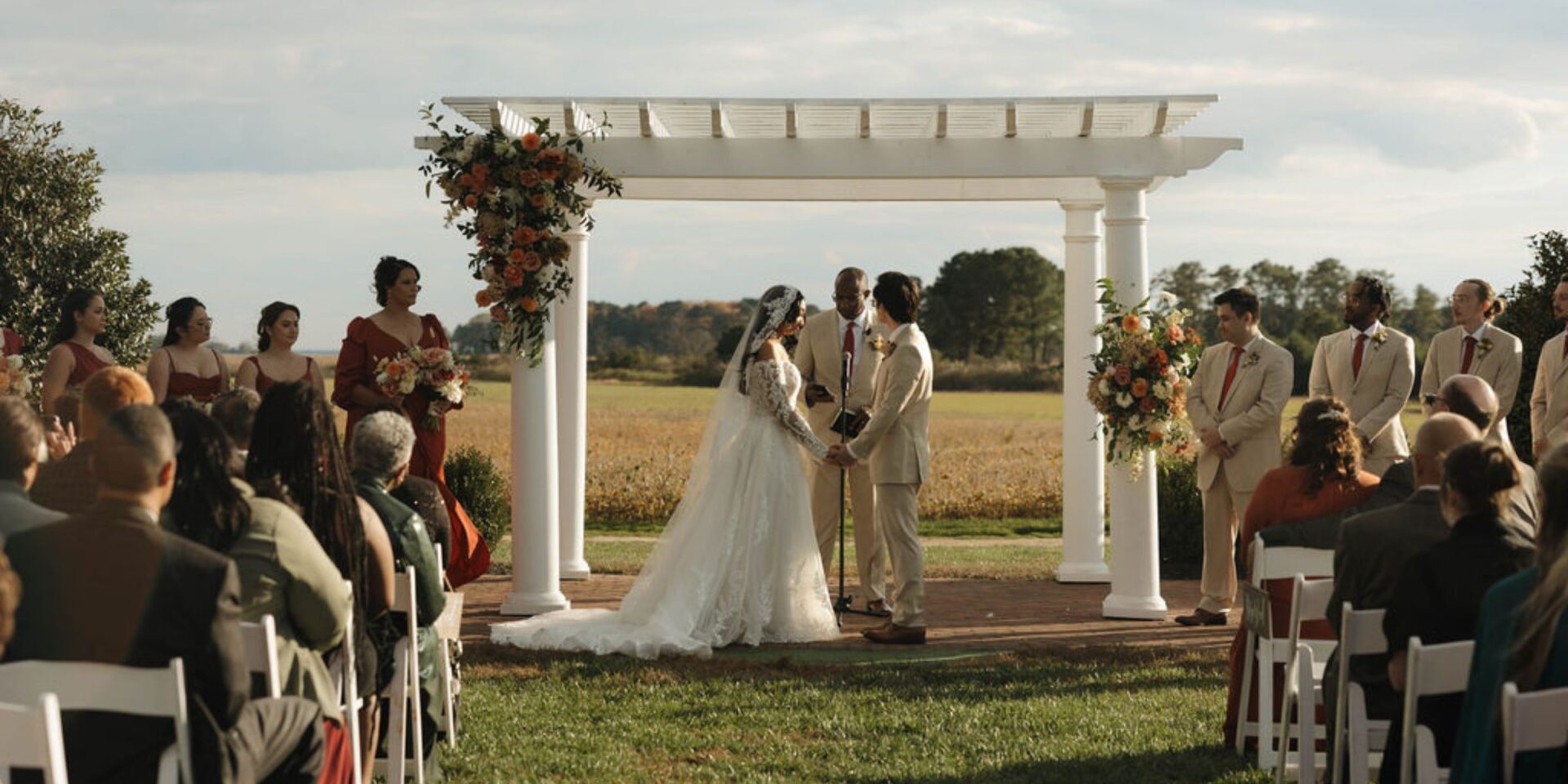 Couple stands for wedding ceremony under white pergola arch.