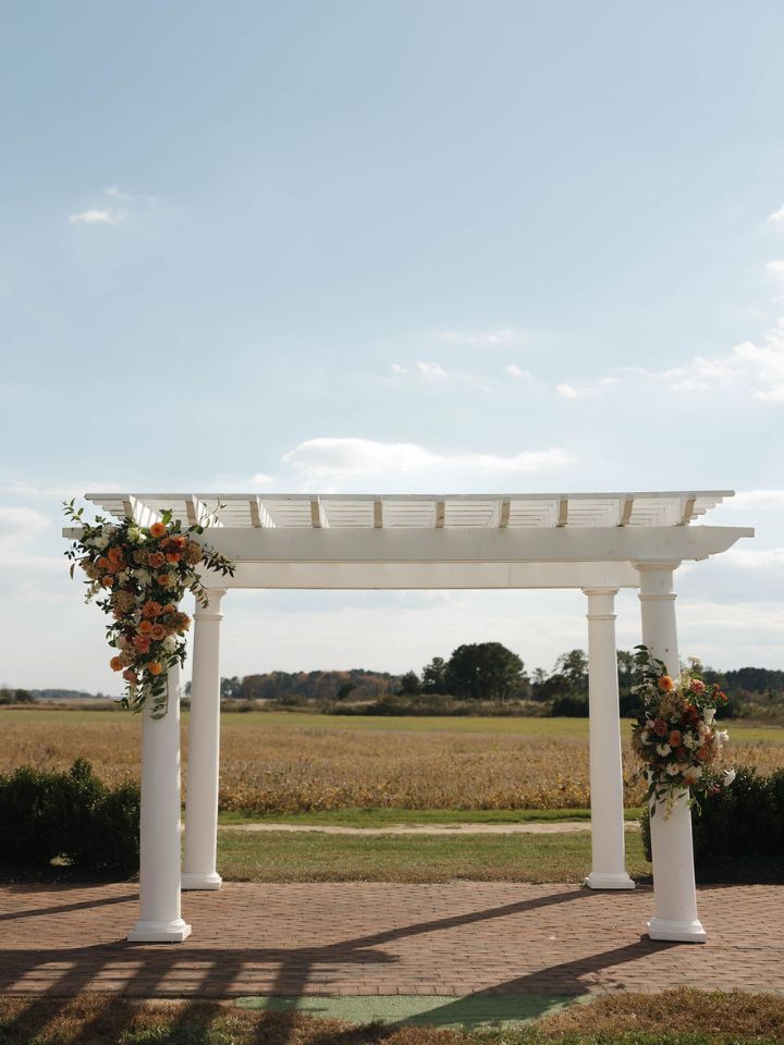 White pergola at Kent Island Resort with simple sized flower arrangements in fall colors for an October wedding.