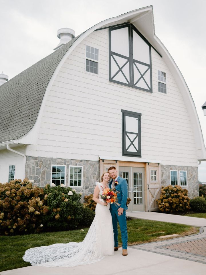 Bride and groom stand in front of barn.