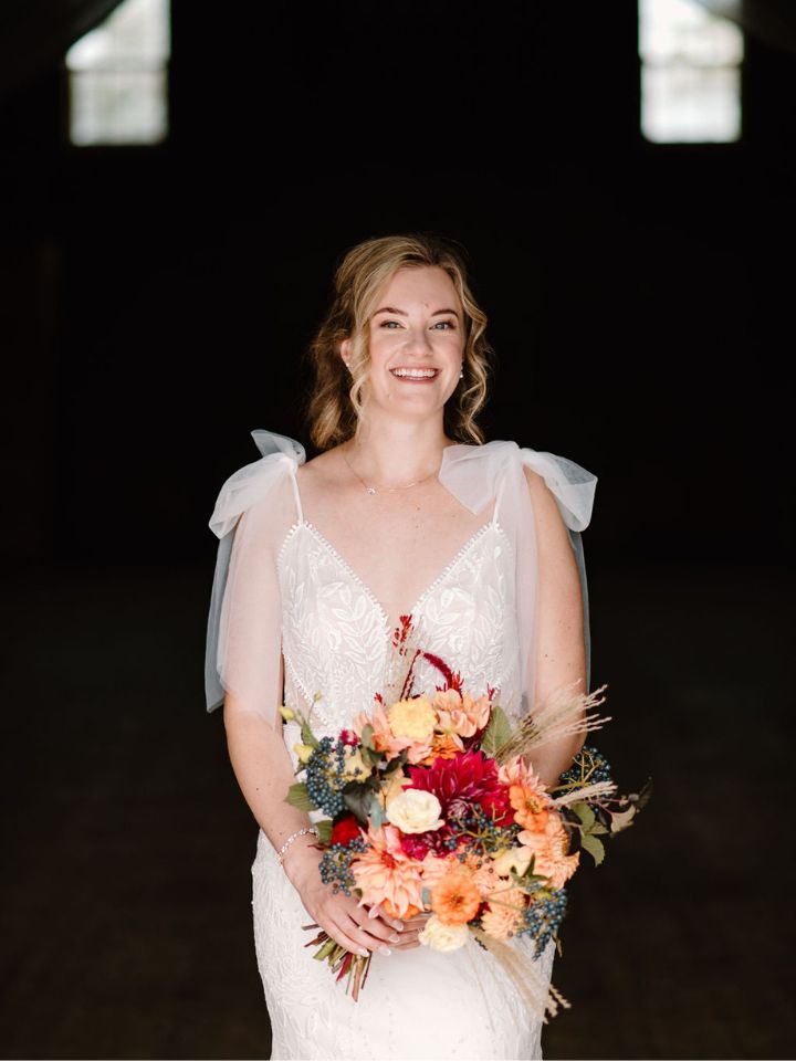 Bride poses inside the barn with her fall flower bouquet.