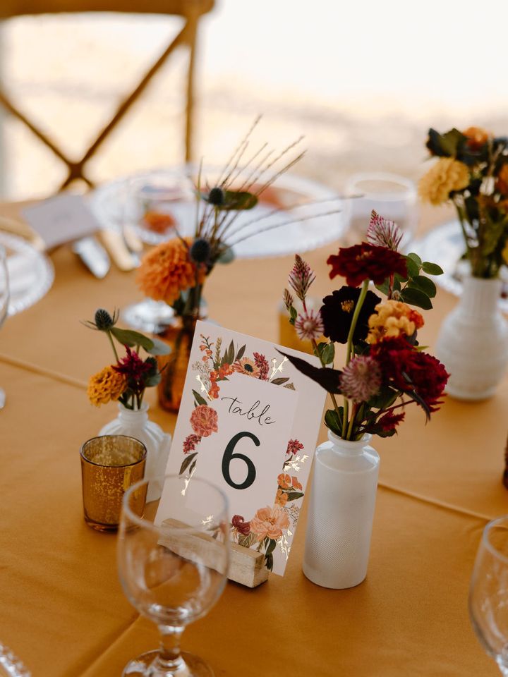 Mustard yellow table cloth with centerpiece of bud vases with fall color flowers.