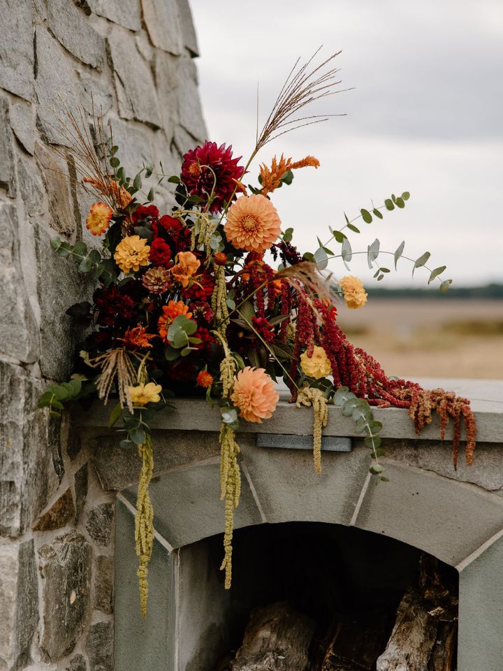 Fall flower arrangement sits on side of large outdoor stone fireplace.