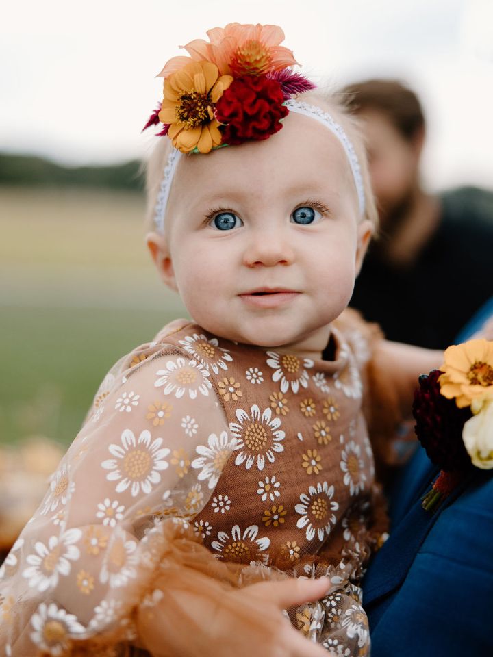 Flower girl in brown and orange flower print dress wears a stretchy headband with fall flowers.