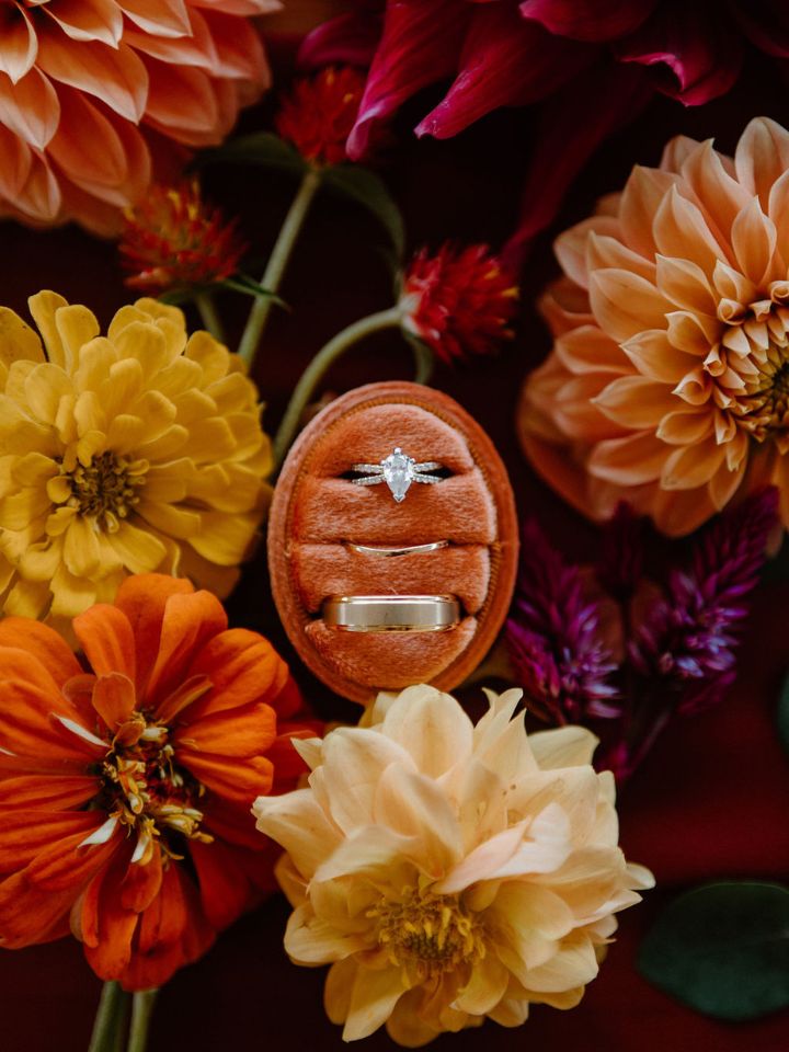 Wedding rings in a rust orange velvet ring box, surrounded by fall flowers.