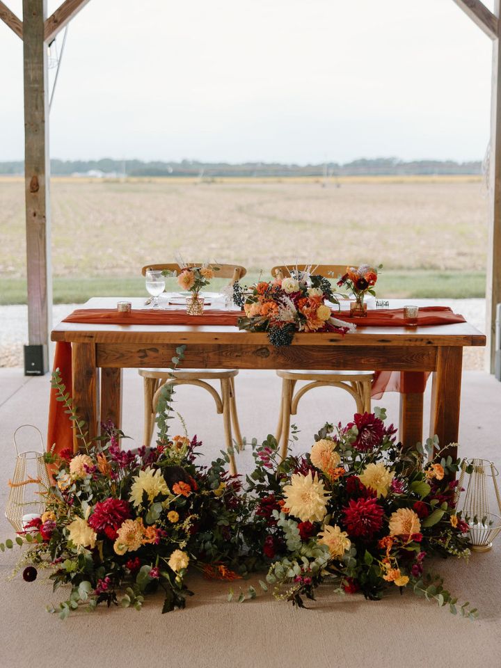 Sweetheart table with fall color flower arrangements at base.