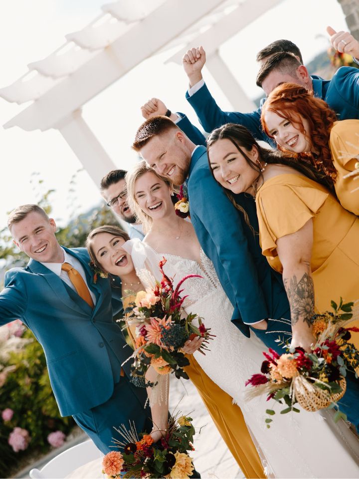 Bride and groom cheer with wedding party in blue suits and mustard gold dresses.