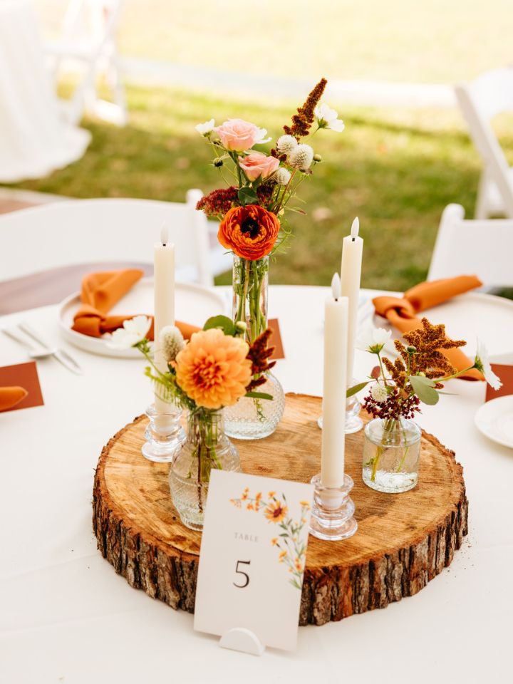 Round table centerpiece with wood slab, and taper candles and bud vases on top.
