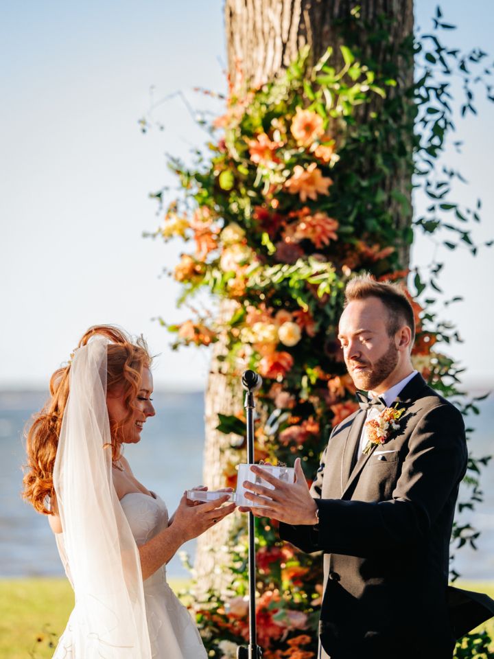 Bride and groom stand at tree covered in flowers for wedding ceremony.