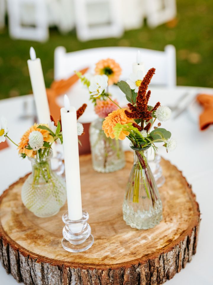 Bud vases with fall flowers and ivory taper candles on top of a wood slab for a table centerpiece.
