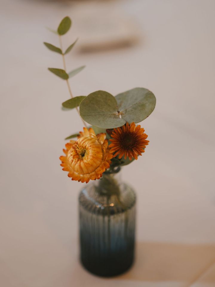 Blue bud vase with orange, yellow, and green flowers.