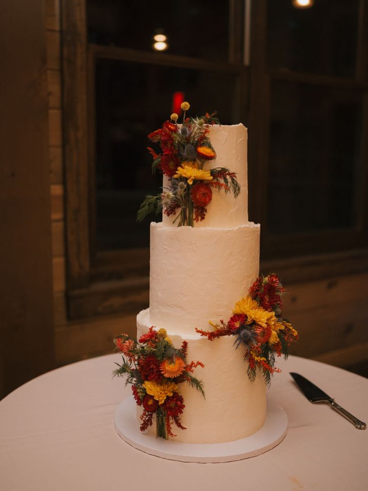 Three tier white wedding cake with fall colored flowers.