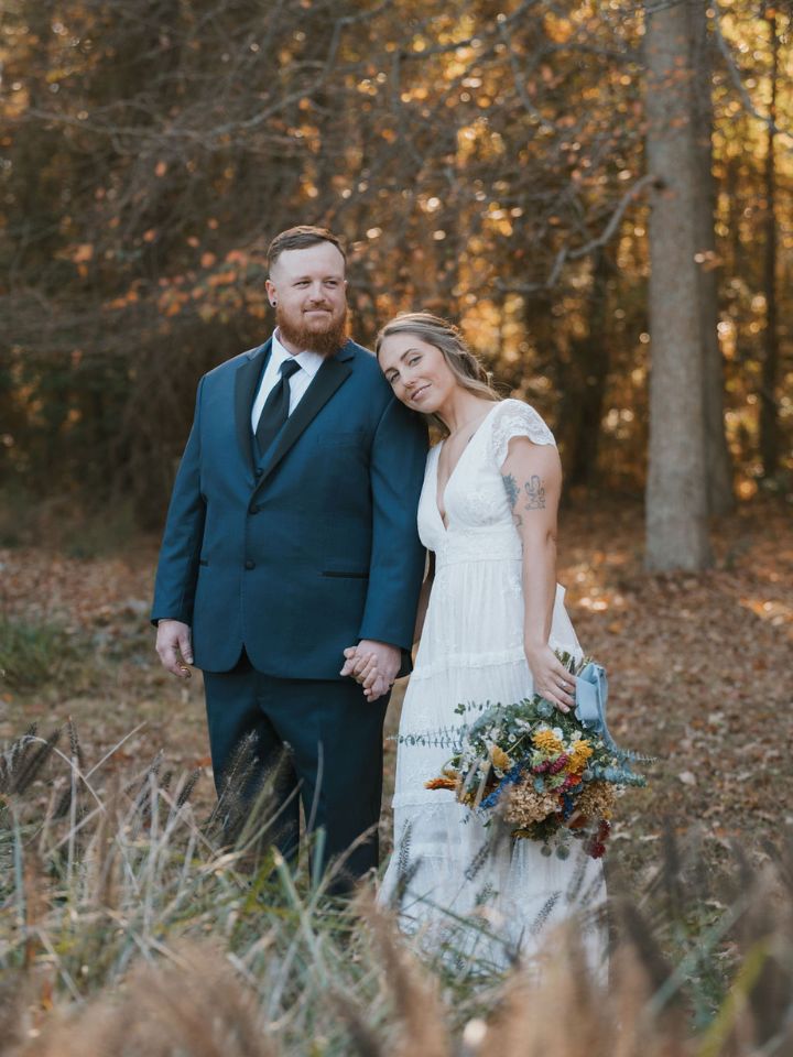 Bride and groom pose with bouquet in woods.