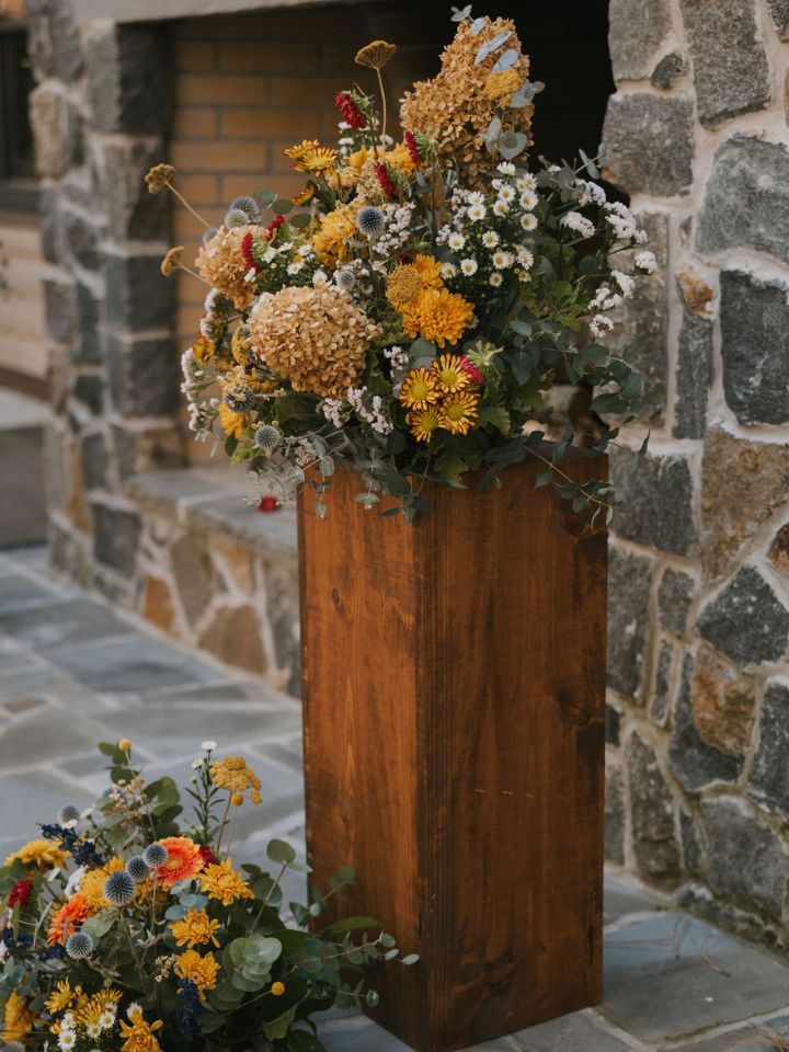 Wooden pedestal with flower arrangement on top.