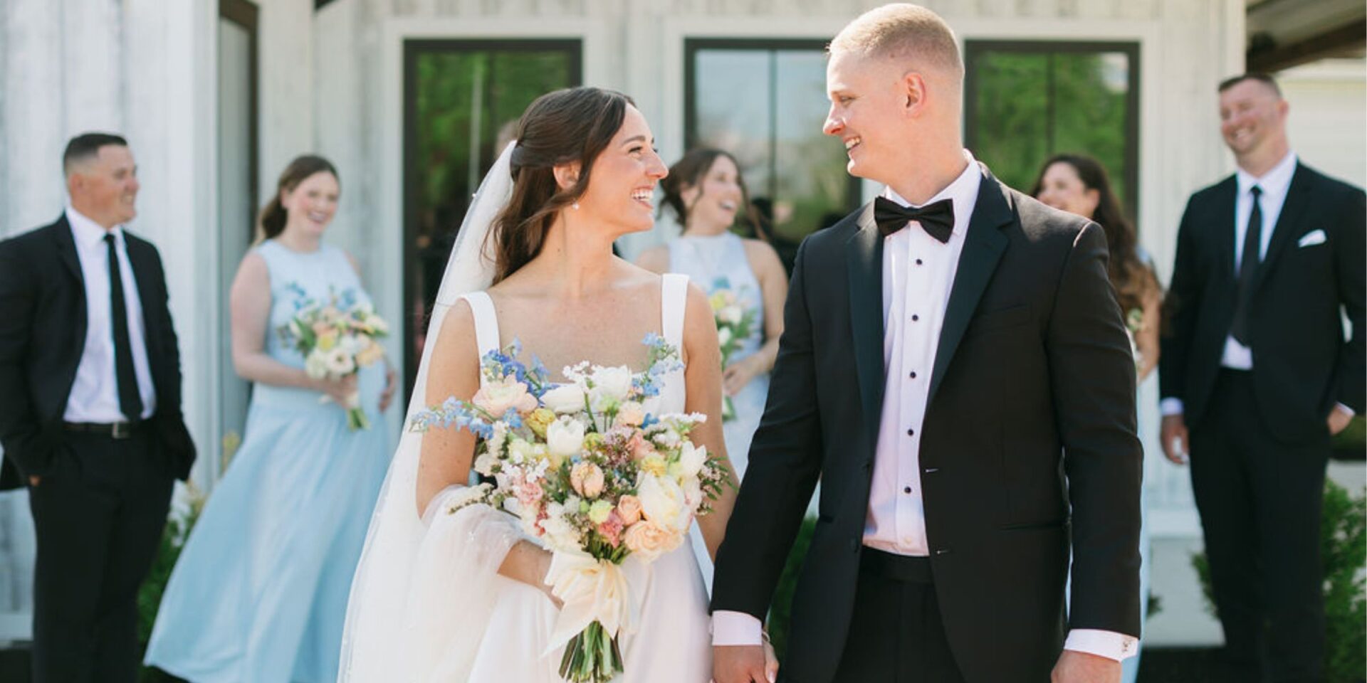 Bride and groom smile at each other in front of wedding party