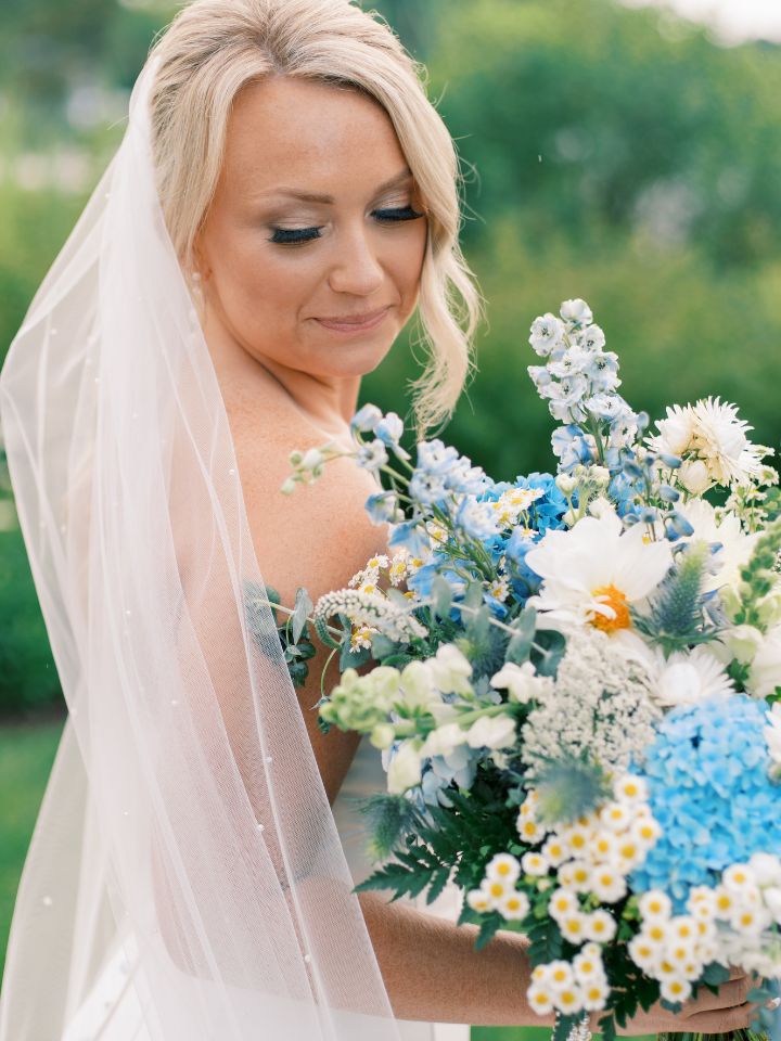 Bride smiles at her blue and white flower bouquet.