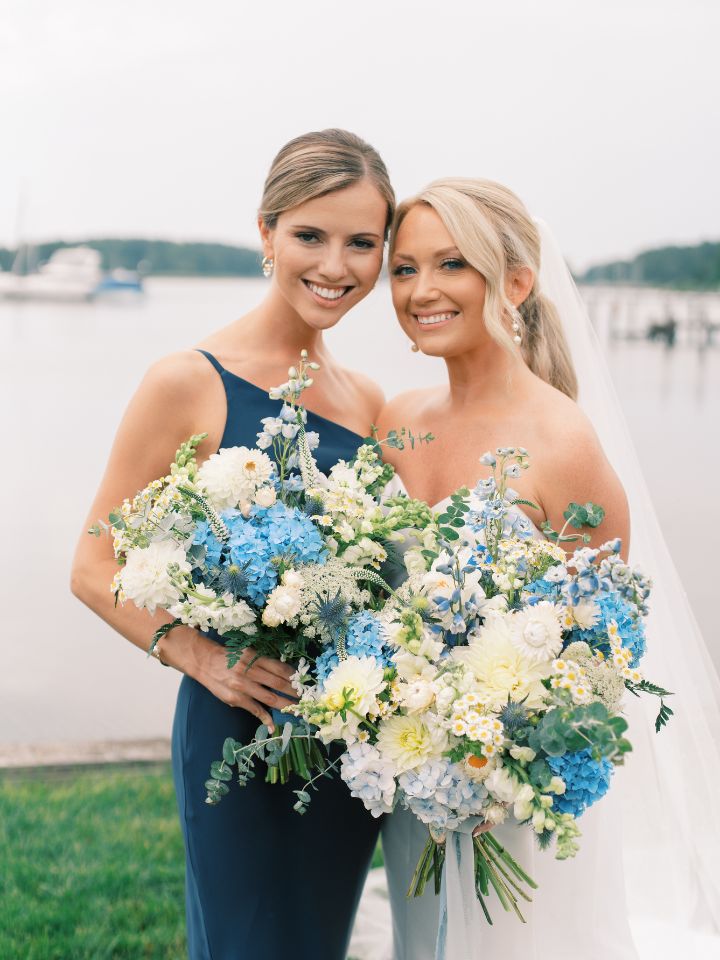 Bride and bridesmaid in navy blue dress hold bouquets.