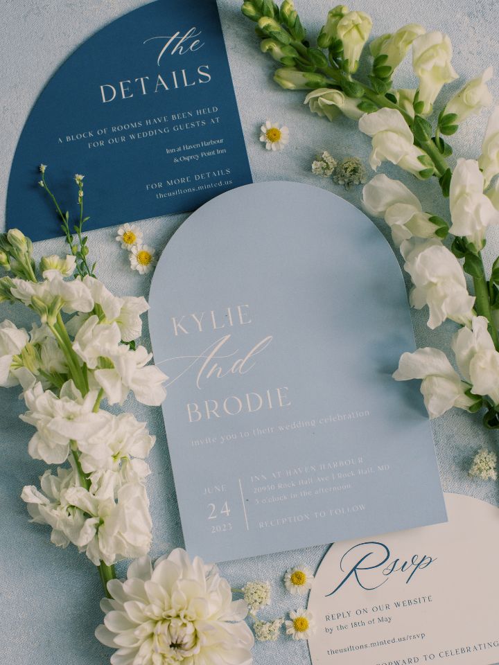 Flat lay photo of blue wedding invitation suite with white summer flowers.