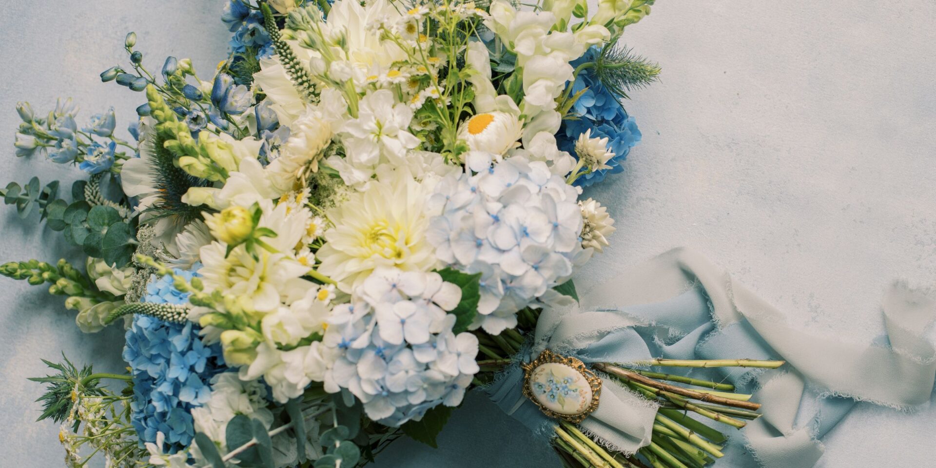 Blue and white bridal bouquet laid on light blue fabric.