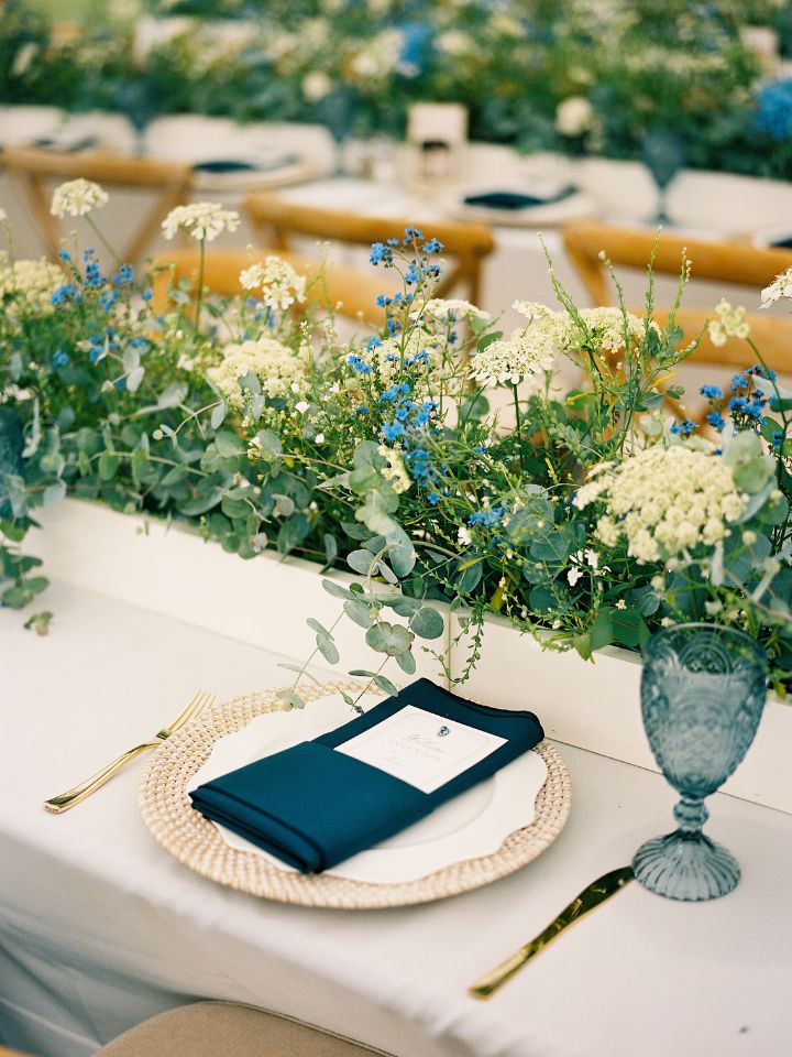 Wedding reception table with long white box full of white and blue flowers.