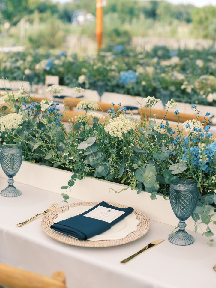 Reception table with white flower box runner, blue glassware, and navy napkins.