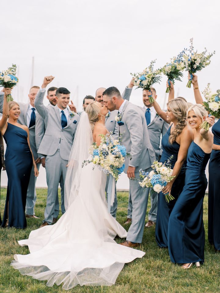 Bride and groom kiss while bridal party cheers.