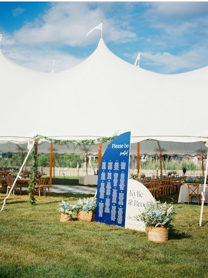 Large blue signage for seating chart at entrance to sailcloth tent reception.