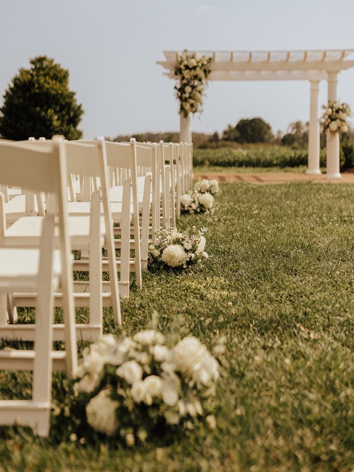 Flower arrangements line the aisle at an outdoor wedding ceremony.