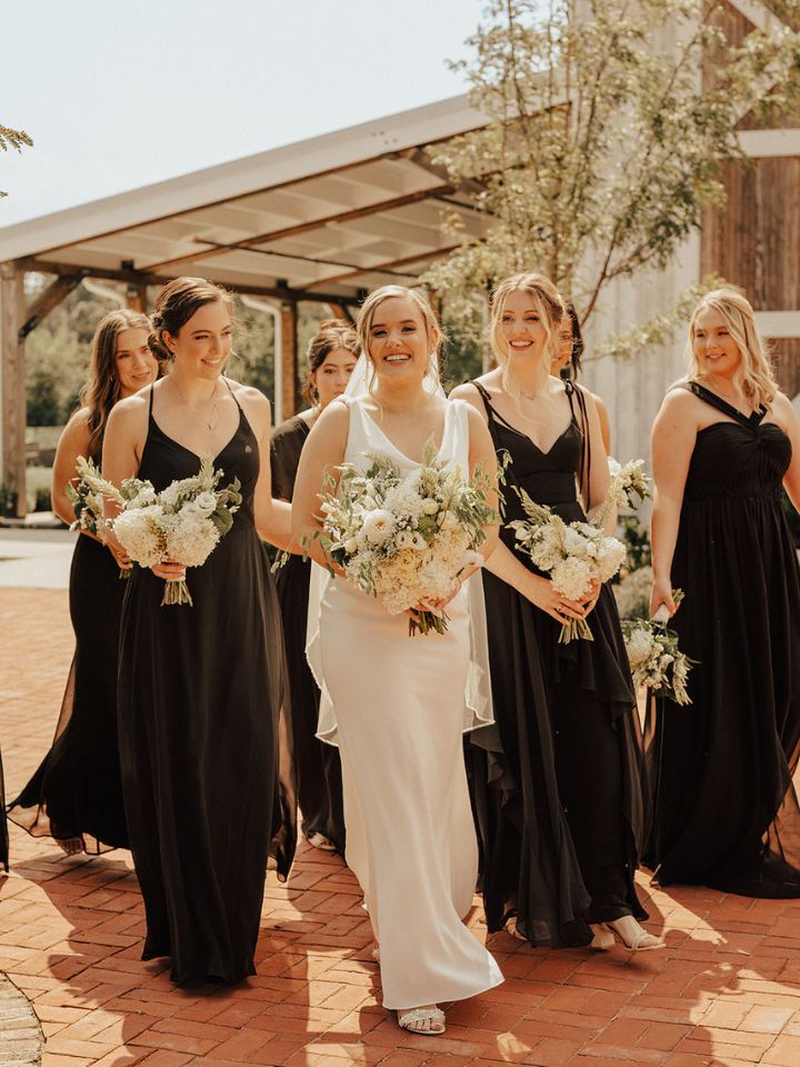 Bride walks with bridesmaids in black dresses.