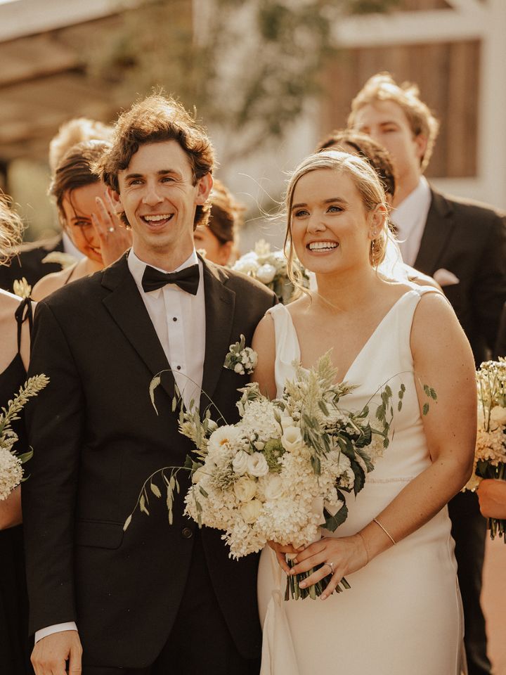 Bride and groom smile towards camera, holding bouquet.